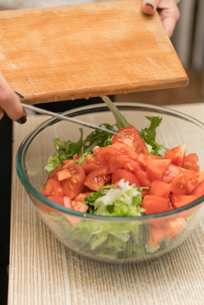 Женщина кладет нарезанные помидоры в салатницу
. - Фото, изображение