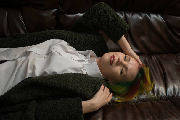 A woman with multi-colored hair is lying on a leather sofa. - Foto, imagen