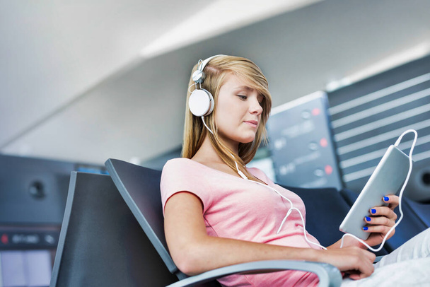 Portrait of young teenage girl sitting while watching movie on her digital tablet with headphones on in airport - Φωτογραφία, εικόνα