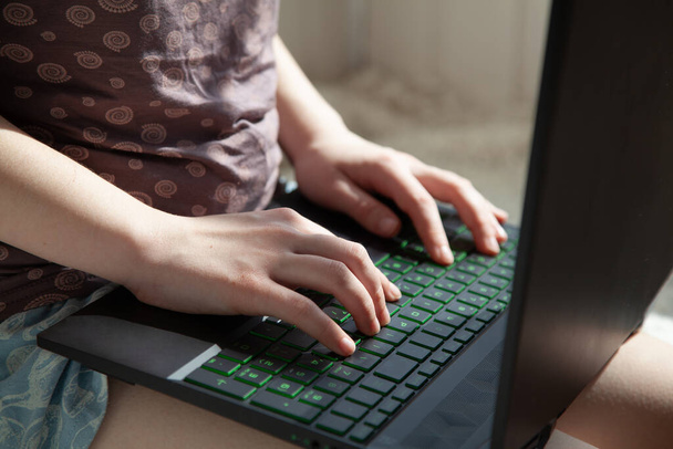 Uma menina em roupas de casa trabalha em casa em um laptop. Trabalho remoto em casa durante o tempo de quarentena.
. - Foto, Imagem