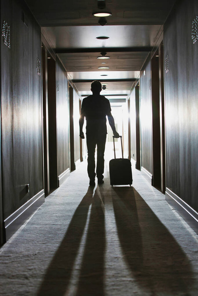 Rear view of man walking with his suit case in hotel - Foto, afbeelding