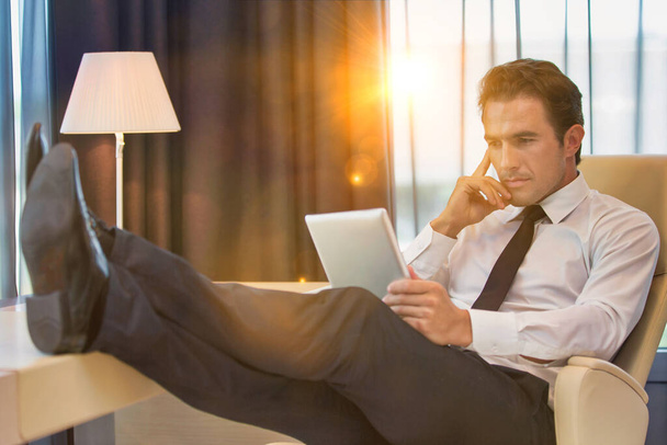 Thoughtful businessman using digital tablet while sitting with lens flare - Foto, Imagem