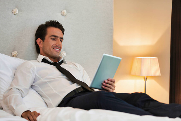 Ώριμος επιχειρηματίας ξαπλωμένος στο κρεβάτι ενώ χρησιμοποιεί ψηφιακή ταμπλέτα στο σπίτι - Φωτογραφία, εικόνα