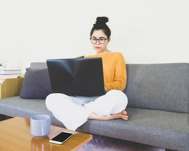 soft selective focus young beautiful asian woman wore orange knitwear,sitting on gray sofa,work online lifestyle,relax at home with coffee,home working laptop,work from home - Фото, изображение