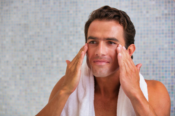 Portrait of attractive man cleansing his face with facial foam in the bathroom - Fotó, kép