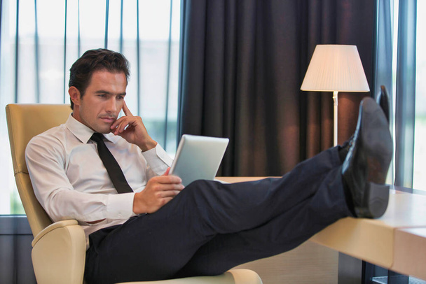Thoughtful businessman using digital tablet while sitting with lens flare - Valokuva, kuva