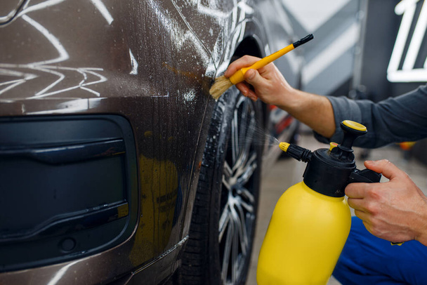 Erkek işçi araba yüzeyini sprey ve fırçayla temizler, koruma filmi uygulamadan önce hazırlık, detay. Araba boyasını çiziklerden koruyan bir kaplama kurulumu - Fotoğraf, Görsel