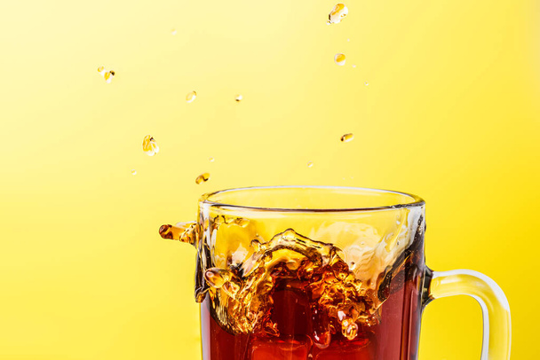 Hot tea in transparent mug on a yellow background splashed wiht ice - Foto, afbeelding