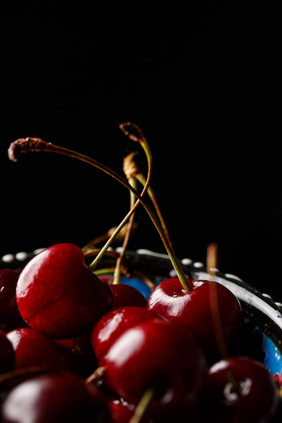 Cherry in a blue bowl close-up on a black background - Foto, Imagen