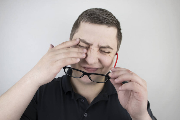 A man rubs his tired eyes with his hands on a white background. The concept of eye fatigue from the computer and fatigue from work. Pain in the eyes and forehead, migraine, eye diseases - Photo, Image
