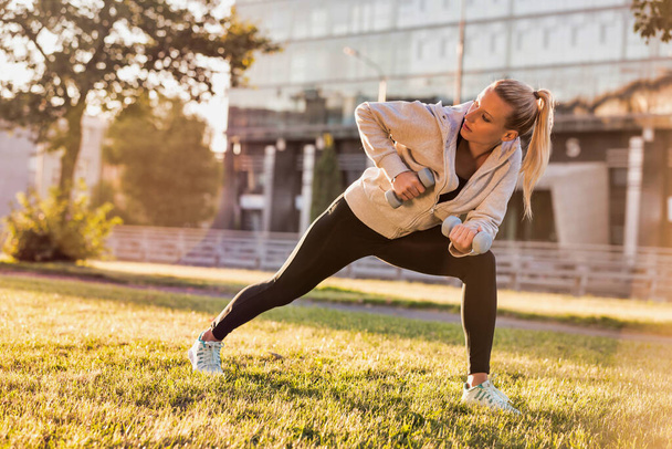 Young attractive woman stretching in park with dumbbells - Fotografie, Obrázek