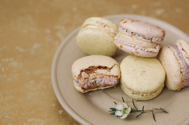 Yellow homemade macarons with blossom are lying on the brown plate on the golden background. - Foto, Bild