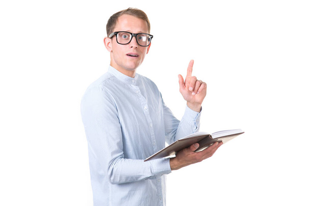 Idea! Young smart man in glasses with a book in his hands raised his finger up, isolated on a white background. - Foto, imagen
