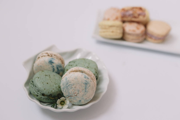 Les macarons faits maison sont couchés sur la plaque blanche sur fond blanc avec des macarons verts et blancs dans l'assiette
 - Photo, image