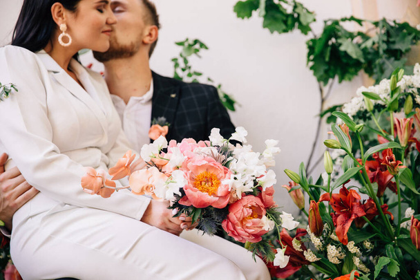 the bride and groom gently posing between floral arrangements of fresh flowers in color coral created for an outdoor wedding ceremony - Foto, imagen