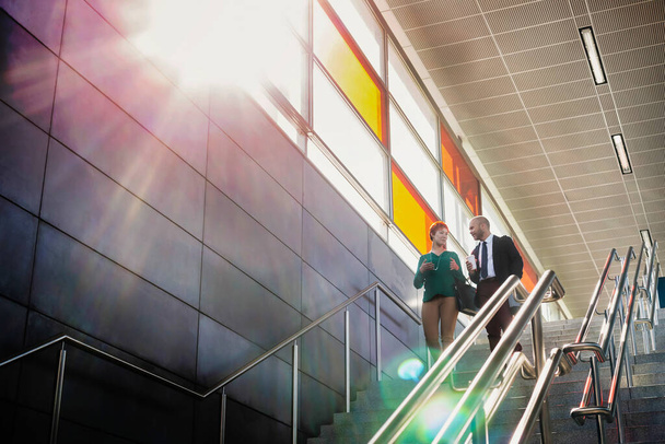 Portrait of businessman and businesswoman talking while walking down stairs - Fotoğraf, Görsel