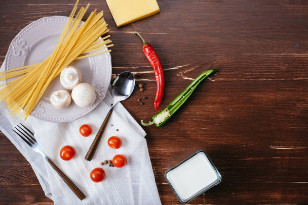 Zutaten für Pasta auf einem Holztisch. Teller, Besteck, Nudeln und frisches Gemüse von oben - Foto, Bild