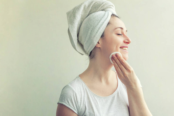 Piękny portret uśmiechniętej kobiety w ręczniku na głowie z miękką zdrową skórą usuwającą makijaż z bawełnianą podkładką odizolowaną na białym tle. Pielęgnacja skóry oczyszczające spa relaks koncepcja - Zdjęcie, obraz
