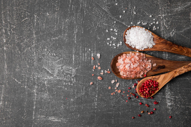 Top view on three wooden spoons with variety of species white sea and pink Himalayan salt and red peppercorn on the scratched grey background on the right side - Fotoğraf, Görsel