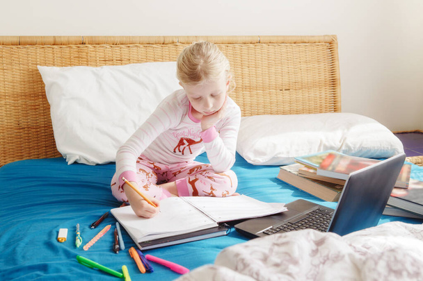 Kaukázusi lány gyermek ül az ágyban, és tanul online laptop interneten. Virtuális osztály lecke iskola video chat közben az önelkülönítés karantén otthon. Távoli videoképzés.  - Fotó, kép