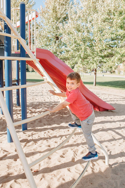 Aktif mutlu beyaz çocuk oyun parkında merdivene tırmanıyor. Yazın güneşli bir günde okul bahçesindeki çocuk. Çocuk dışarıda oyun alanında eğleniyor. Mevsimlik spor çocuk aktiviteleri. - Fotoğraf, Görsel