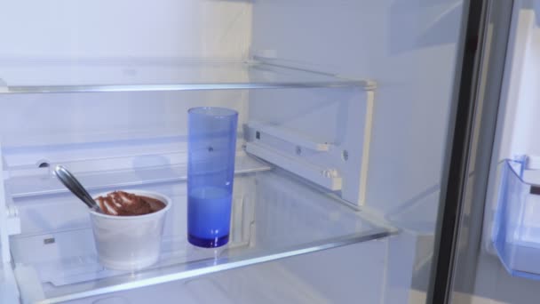 Woman take chocolate pudding and glass of milk from empty fridge - Footage, Video