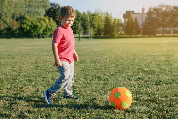 Caucasian boy playing soccer football on playground outside. Preschool kid kicking hitting ball. Happy authentic candid childhood lifestyle. Seasonal summer outdoor activity for children. - Photo, Image