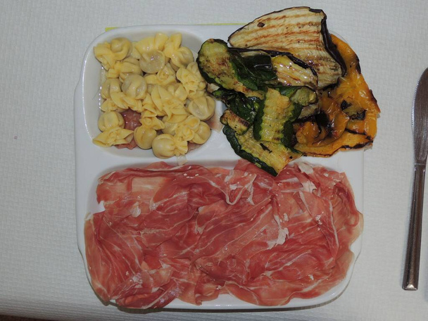Tortelli San Daniele sonkával, vajjal és zsályával fűszerezve, grillezett zöldségekkel és szeletekkel tálalva San Daniele sonkából - Fotó, kép