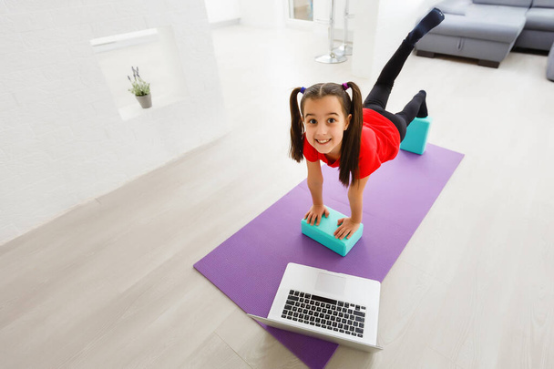 Quarantine at home. little girl doing yoga olnline on a laptop during self isolation quarantine - Foto, immagini