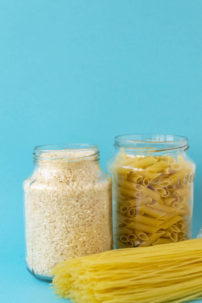 Noodles, rice, pasta in glass jars stand on a blue background. Raw materials for cooking. There is a place for text. - Photo, Image