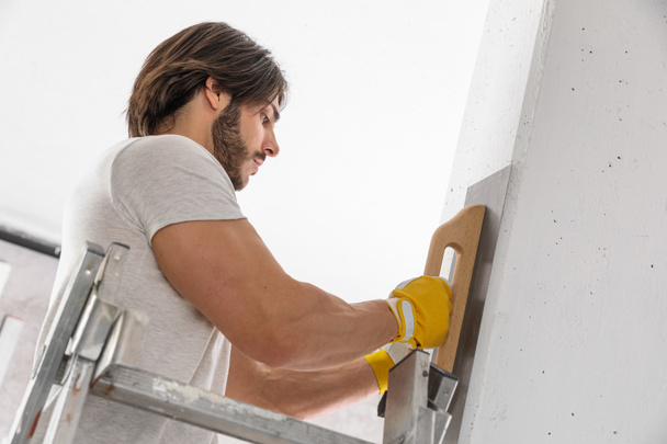 Plasterer finishing the surface of a white wall using a trowel during building or renovations on a house interior - Foto, Imagem