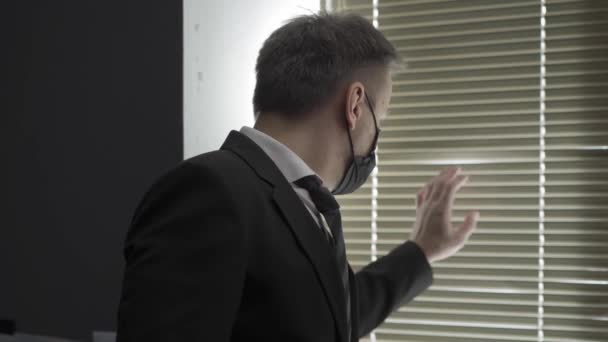 Businessman sadly looking in the window wearing face mask. - Materiał filmowy, wideo
