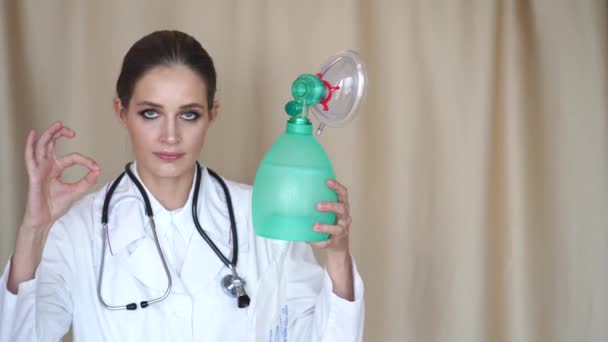 Bir kadın doktor kameraya bakar ve yapay akciğer havalandırma cihazını gösterir ve evde, karantinada, solunum cihazında her şeyin iyi olacağını gösterir. - Video, Çekim