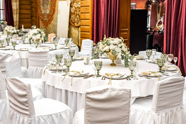 Witte bruiloft decoratie in restaurant. Luxe bruiloft arrangement. Bruiloft banket decoratie. Tafels in restaurant versierd met prachtige witte pioenen en rozen - Foto, afbeelding