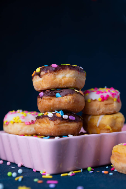 Mini donuts polvilhados empilhados com um fundo escuro
 - Foto, Imagem