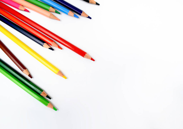 Buntstifte in verschiedenen Farben sind zufällig auf einem strahlend weißen Hintergrund verstreut - Foto, Bild