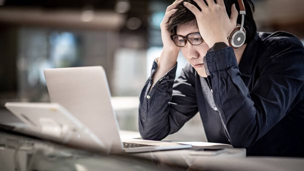 自宅のノートパソコンで仕事をしながら、アジアのビジネスマンはストレスや頭痛を感じていました。男性起業家は仕事上の問題に悩まされている。経済危機の概念. - 写真・画像