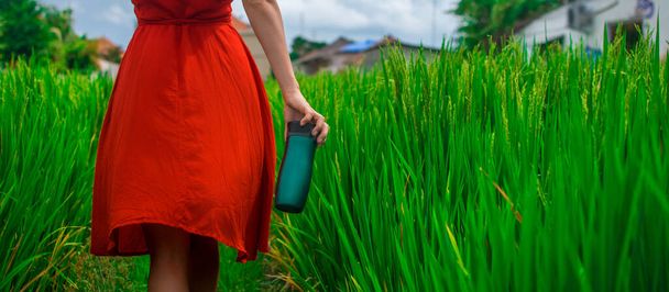 Beautiful young woman walking in red dress.Isolated on green natural background.Hand holding hot cup mug. Азиатский склон с рисоводством, зеленые каскадные рисовые поля в форме гор террасы
. - Фото, изображение