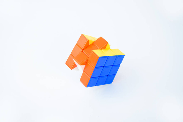 Ein gelöster Rubik 's Cube auf weißem Hintergrund mit leuchtend blauer, oranger und gelber Farbe - Foto, Bild