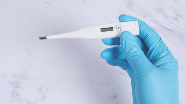 Digital thermometer white color in doctor hands wearing hospital medical gloves light blue color which can shown checking temperature numbers in celsius or fahrenheit degree for pandemic fever - Foto, afbeelding