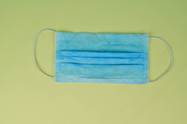 Açık sarı kağıtta izole edilmiş plastik kayışlı mavi cerrahi maske. - Fotoğraf, Görsel