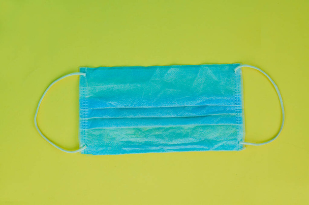 Sarı kağıtta izole edilmiş plastik kayışlı mavi cerrahi maske. - Fotoğraf, Görsel