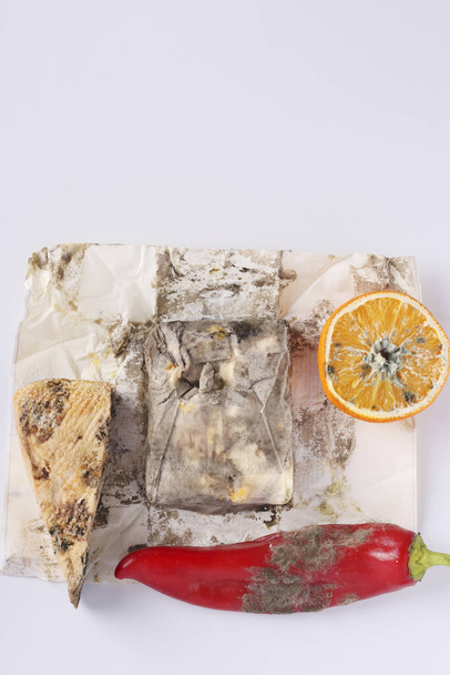 Alimentos podridos estropeados con moho: naranja, pimienta, queso duro y mantequilla sobre fondo blanco, Vista superior, Formato vertical
 - Foto, Imagen