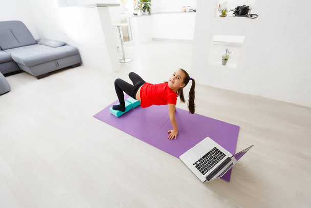 Cuarentena en casa. niña haciendo yoga olnline en un ordenador portátil durante la cuarentena de autoaislamiento - Foto, imagen