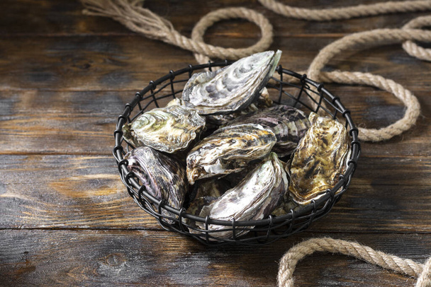 Lots of oysters in a black metal basket on a brown wooden table. Rustic style. French cuisine - Foto, Imagen