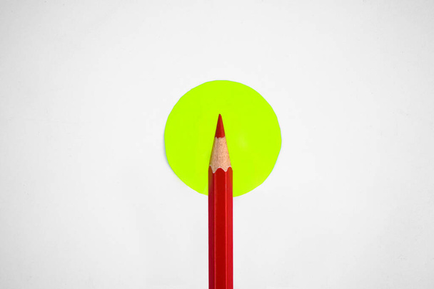 Lápis vermelho único colocado sobre um pequeno círculo amarelo meio de um fundo branco vazio
 - Foto, Imagem
