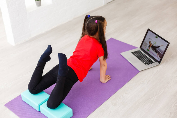Cuarentena en casa. niña haciendo yoga olnline en un ordenador portátil durante la cuarentena de autoaislamiento - Foto, imagen
