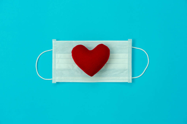 Table top view aerial image of accessories healthcare & medical background concept.Essential equipment tools mask on red love heart on blue paper.Flat lay essential items for protect viral Covid-19. - Photo, Image