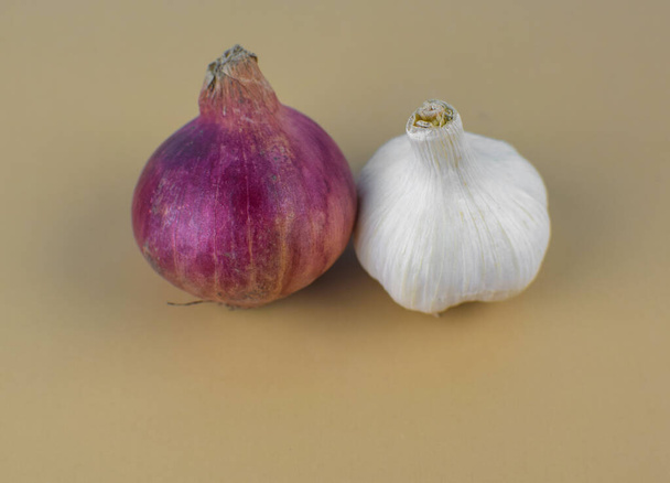 A medium size red onion and a medium size white colored garlic placed beside one another in front a brown background - Foto, afbeelding
