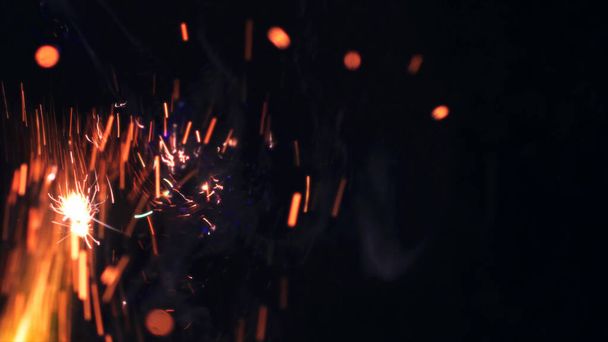 Macro photo of Bonfire sparks. Fire Flames bursts, blasts. Explosion micro sparkles. Mini Fireworks. Shooting on Red camera still on black background. Beautiful leaks overlay spark poster, banner, wallpaper, backdrop, texture. - Photo, Image